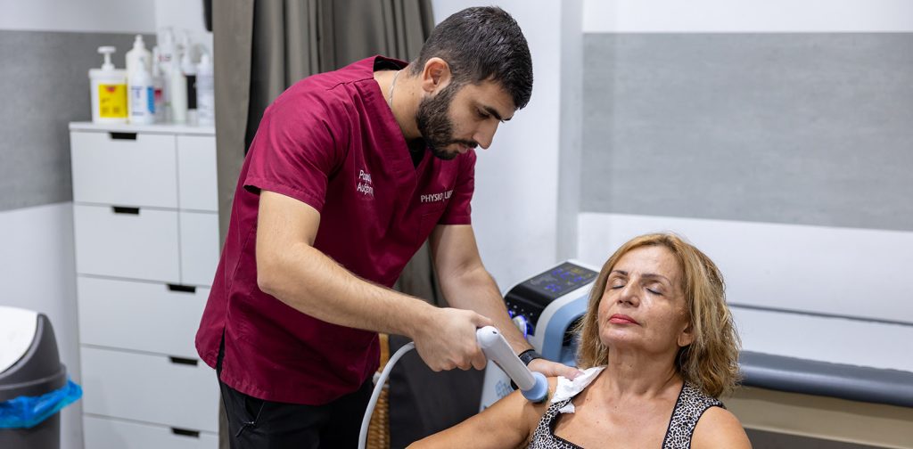 Physiolife therapist using a handheld treatment device on a patient shoulder